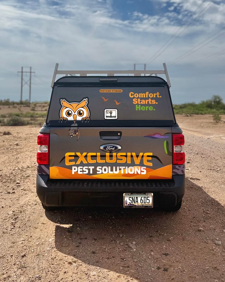 Rear of the Exclusive Pest Solutions truck with Olly the owl on the window, parked on a desert road.